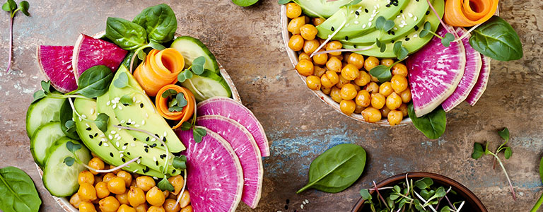 A plant-based salad bowl with chickpeas, avocado, carrot, cucumbers and radishes.